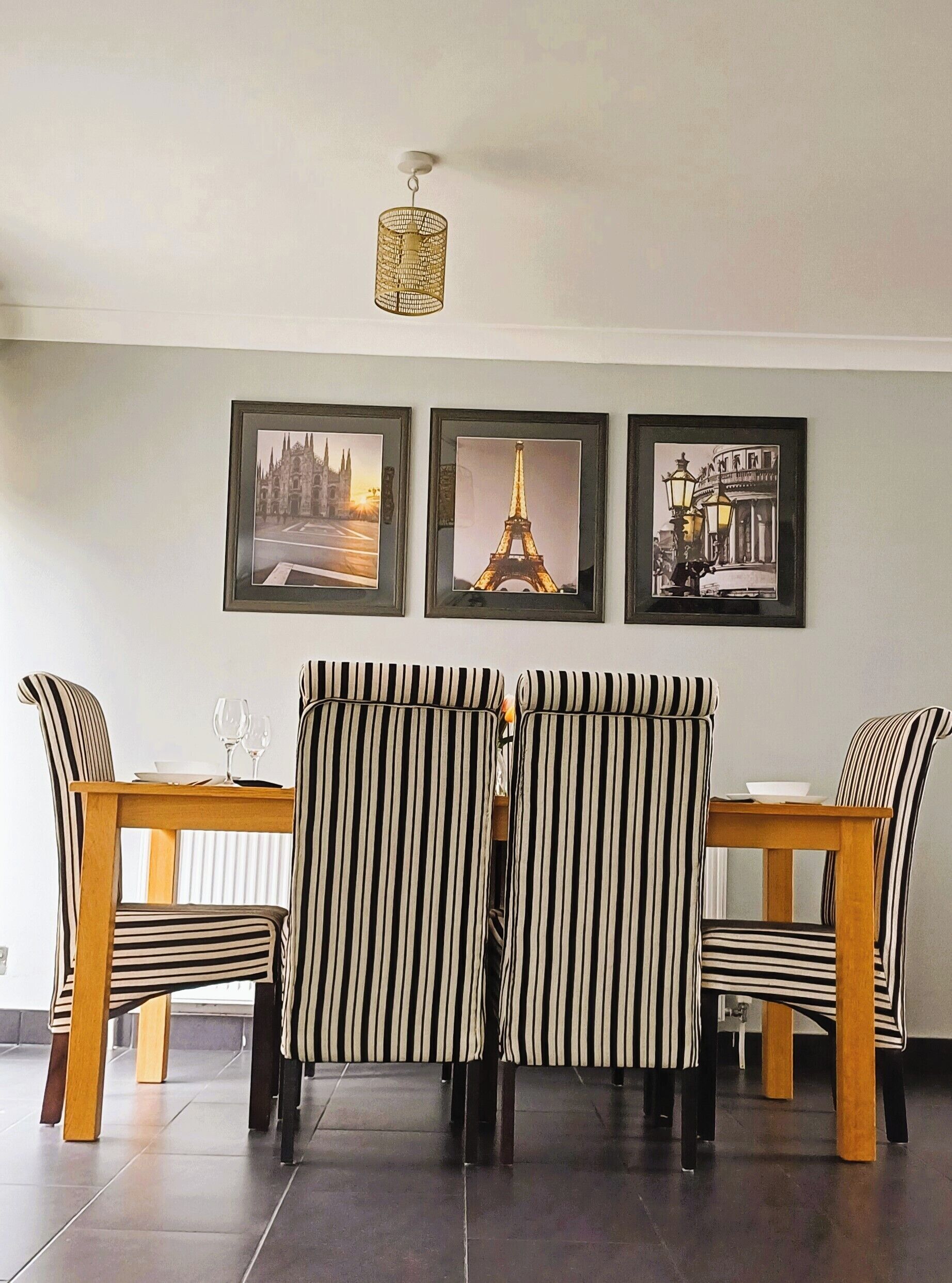 A dining area with a table and chairs, framed pictures on the wall, and a hanging light fixture.