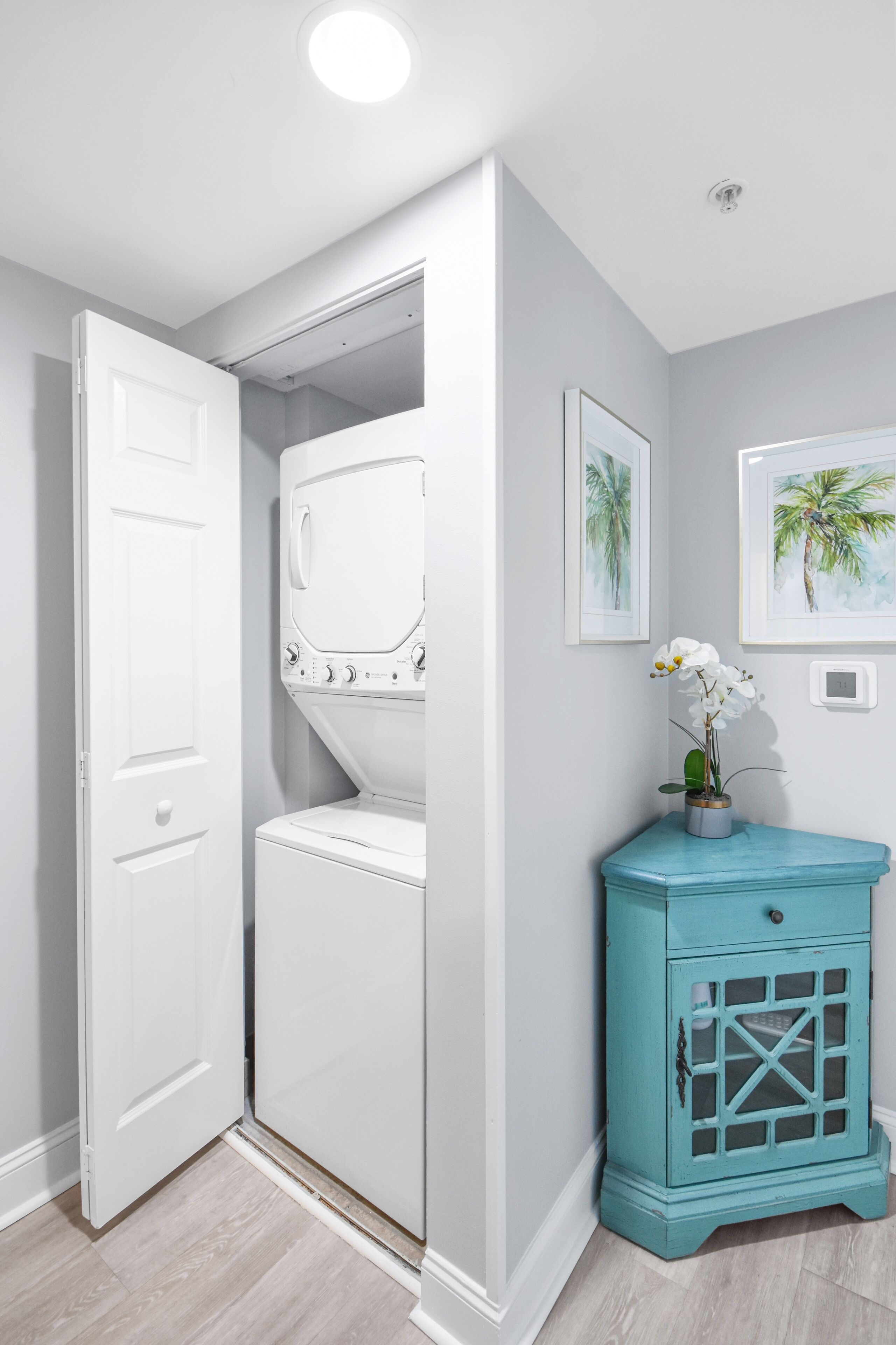Une buanderie avec un lave-linge et un sèche-linge blancs, un meuble de couleur turquoise et deux tableaux encadrés accrochés au mur.