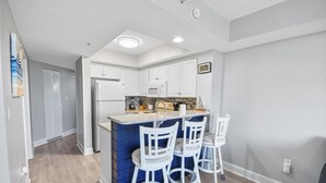A modern kitchen with a central island, white bar stools, and a microwave. - Southwind 204 1 Bedroom Condo (Myrtle Beach)