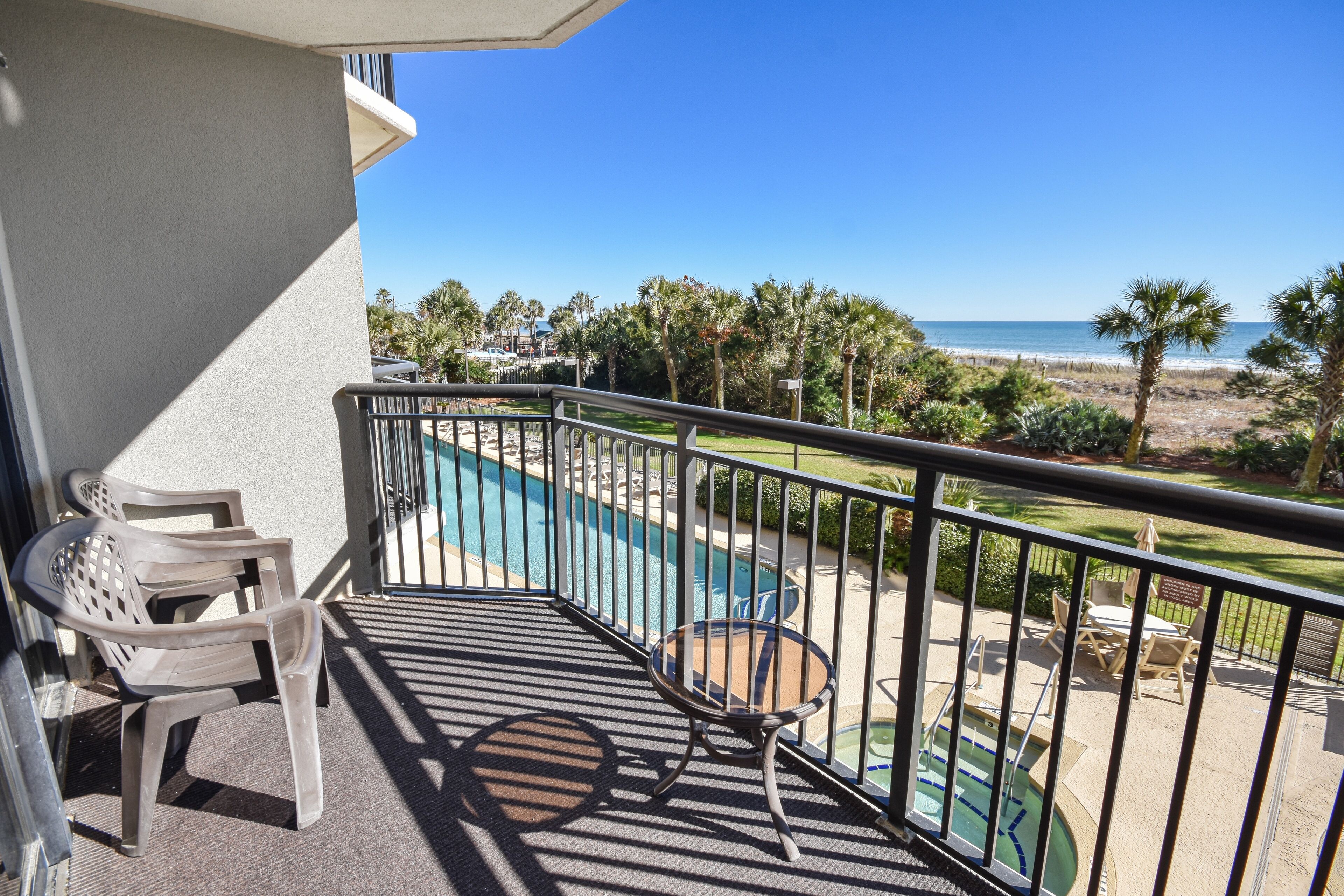 A balcony with a pool, chairs, and a view of the beach.