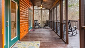 Une cabane en bois avec une véranda, un ventilateur de plafond et une vue sur les arbres.