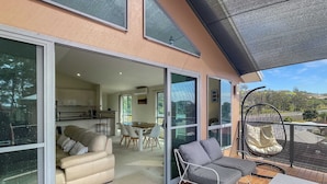 Una casa moderna con un balcón amplio, un comedor y una cocina visibles a través de grandes puertas de cristal.