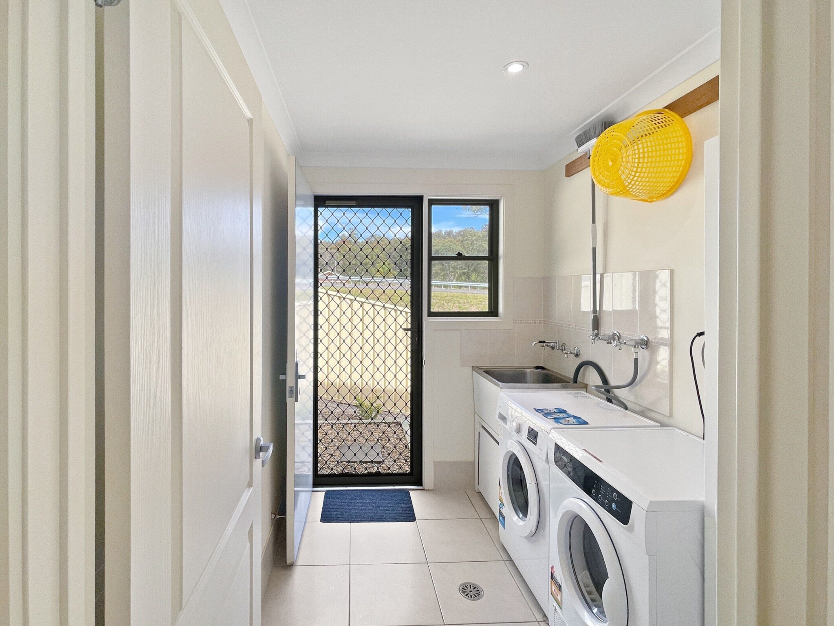 A laundry room with a washing machine, dryer, sink, and a yellow drying rack.
