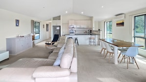 Un espacio habitable amplio con un sofá blanco grande, una mesa de comedor con sillas, una zona de cocina y ventanas grandes que ofrecen luz natural.