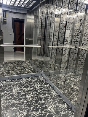 Ein Aufzug mit gemustertem Boden, metallischen Wänden und einer Tür mit Holzverkleidung.