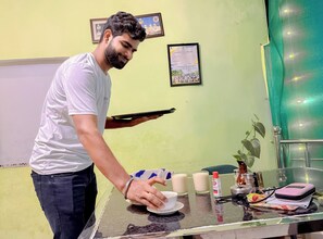Una persona sirviendo una bebida en una barra con una bandeja. La barra tiene un vaso, una botella y un recipiente pequeño. Hay diplomas enmarcados en la pared de fondo.