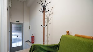 A hotel room with a wooden bed, a green throw, a coat rack, a fire extinguisher, and a door with a window.