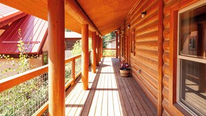 A covered wooden deck with a view of a red-roofed building. - Almost Heaven - Newly Built! - In Town - On the River - WiFi - Grill - Mountain (Red River)