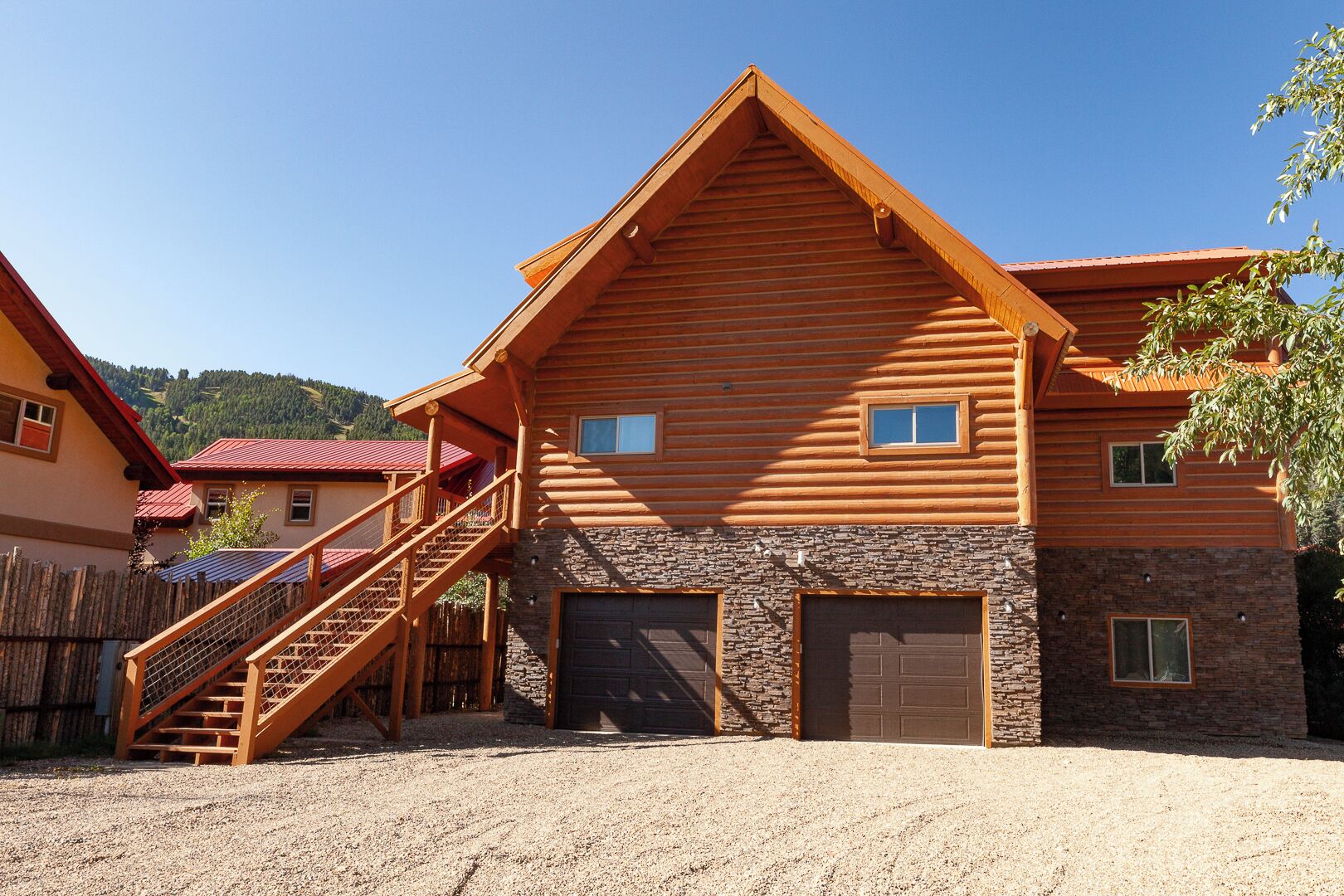A log cabin with a stone foundation, a wooden staircase, and two garage doors.