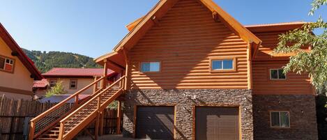 A log cabin with a stone foundation, a wooden staircase, and two garage doors.
