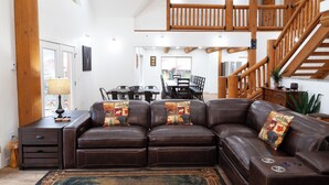 A spacious living room with a brown leather sectional sofa, a dining area with a table and chairs, and a wooden staircase. - Almost Heaven - Newly Built! - In Town - On the River - WiFi - Grill - Mountain (Red River)