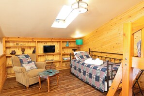 Una habitación acogedora con una cama, una silla, una mesita, televisión y paredes de madera.
