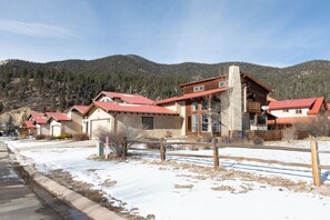 Una hilera de cabañas rústicas con techos rojos, frente a un paisaje de terreno nevado y montañas.