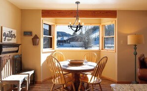 Comedor con una mesa redonda, sillas de madera, una araña y vistas de un paisaje nevado a través de grandes ventanales.
