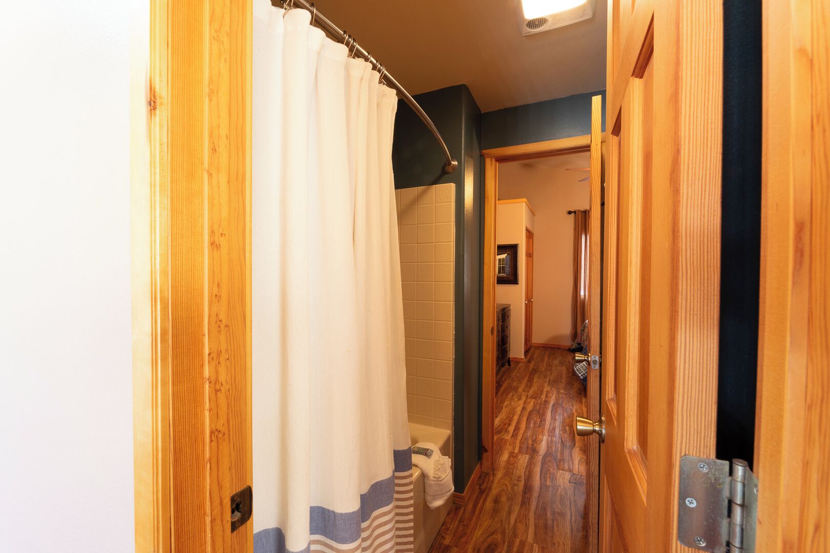 A wooden hallway with a shower curtain, a tiled wall, and a door leading to another room.