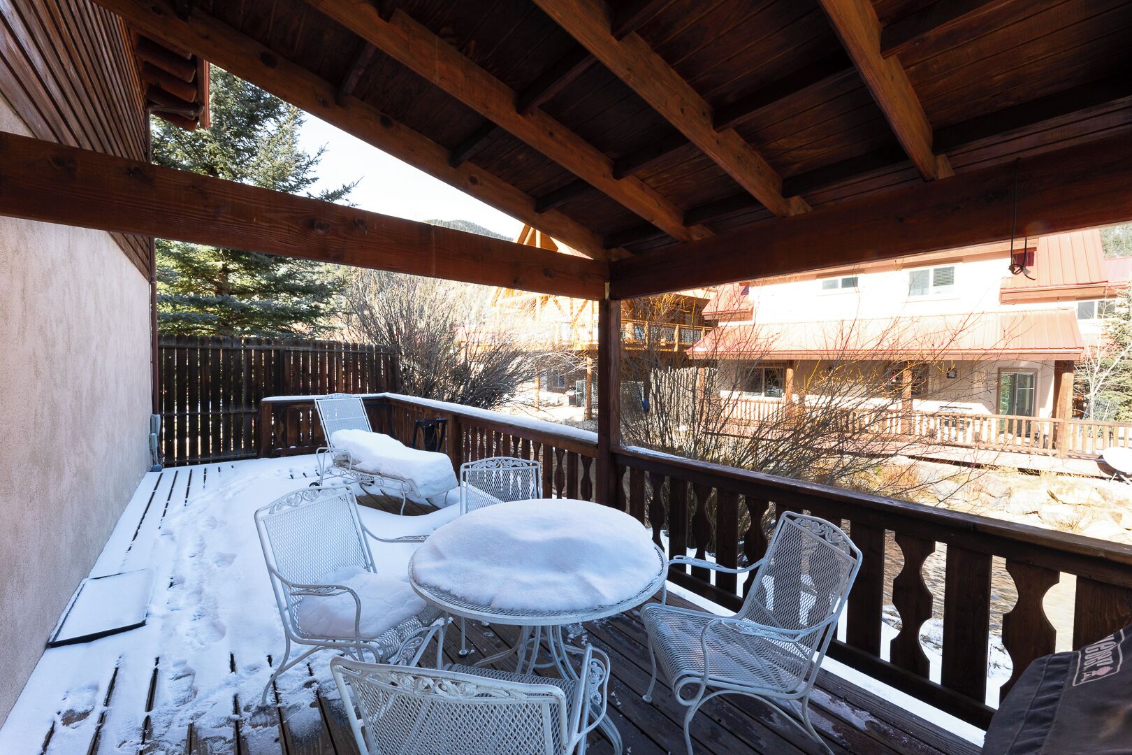 A wooden deck with a table and chairs covered in snow, overlooking a residential area.