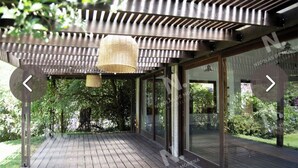 A modern outdoor deck with a wooden floor, large glass windows, and a woven ceiling light fixture.