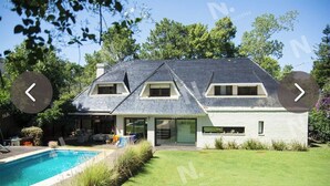 A modern house with a swimming pool, a covered patio, and a well-maintained lawn.