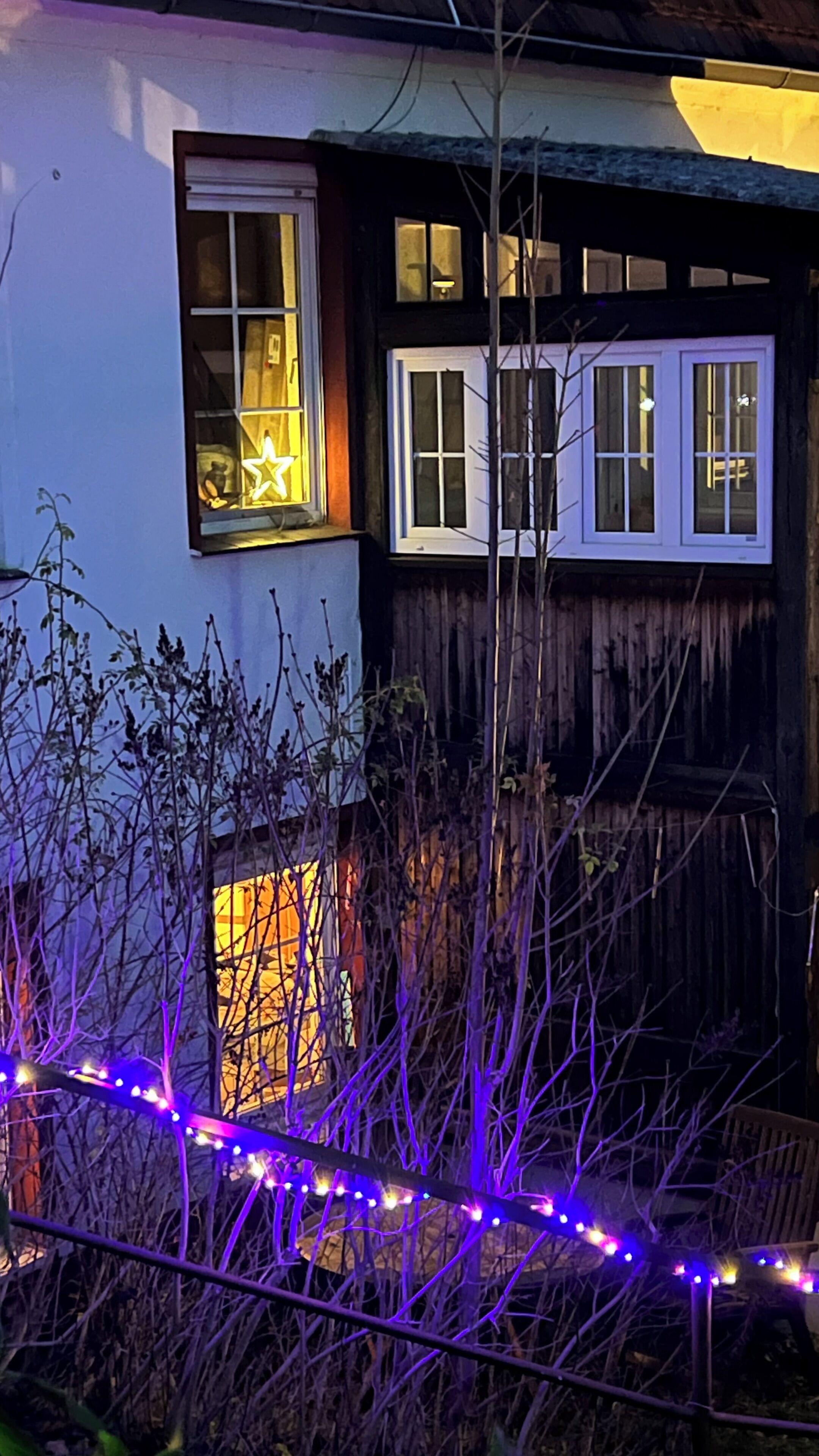 Een huis met twee ramen, waarvan er één een sterdecoratie heeft, en een houten hek op de voorgrond.