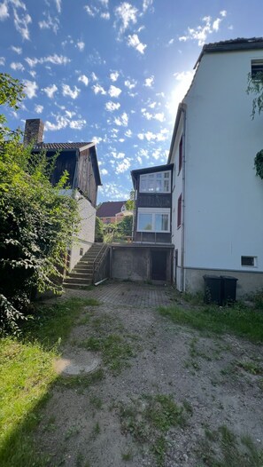 Um bairro residencial com uma trilha de terra que leva a uma casa com escada de madeira e chaminé de tijolos.