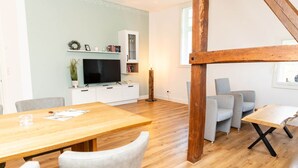 Una sala moderna con una mesa de comedor de madera, sofás grises y un televisor sobre un mueble blanco.