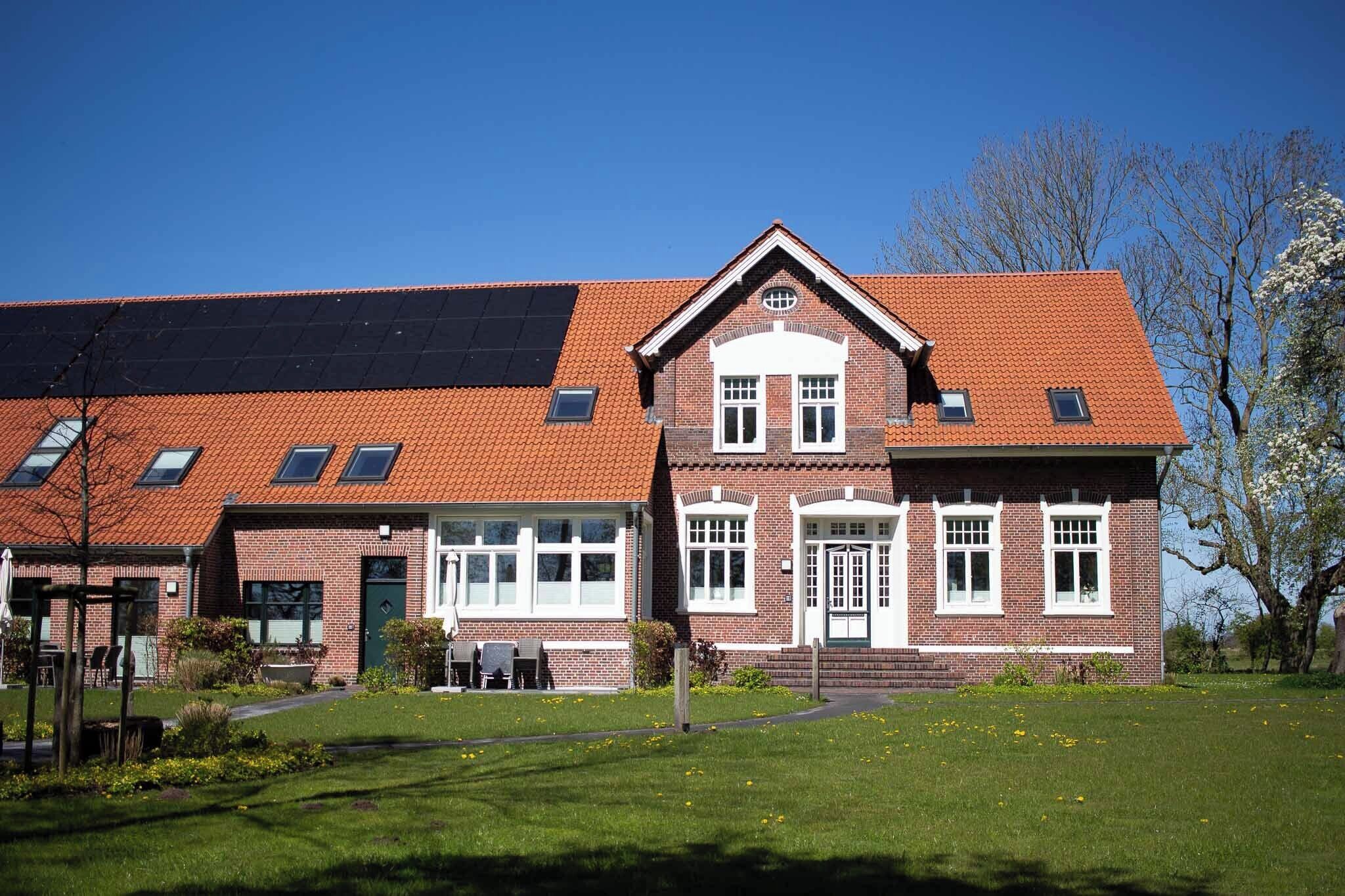 A two-story brick building with a red-tiled roof, large windows, and a green door.