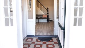 En gang med et mønstret gulv, en trappe med gelænder i sort og en dør med sandblæste glasruder.