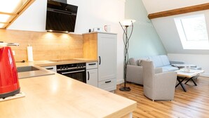 A compact kitchen with a built-in oven and a dining area with a grey sofa and a small table. - Graf Enno | Cozy Two-Level Apartment | North Sea (Norden)