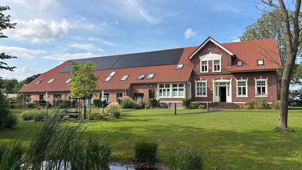Ein großes Ziegelhaus mit geneigtem Dach, zahlreichen Fenstern und einem gepflegten Rasen.
