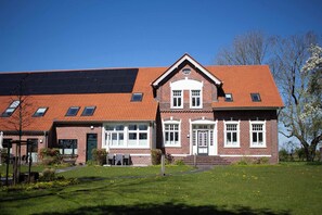 A two-story brick building with a red-tiled roof, large windows, and a green door. - Juliane | Charming apartment with a picture window | North Sea (Norden)