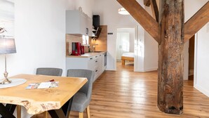 Cozinha moderna com vigas de madeira, mesa de jantar com cadeiras e vista para um quarto.