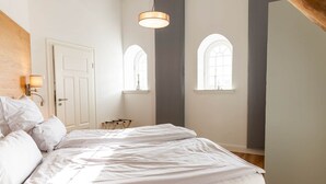 Quarto com cama, mesa de cabeceira, janela e luminária fixada na parede.