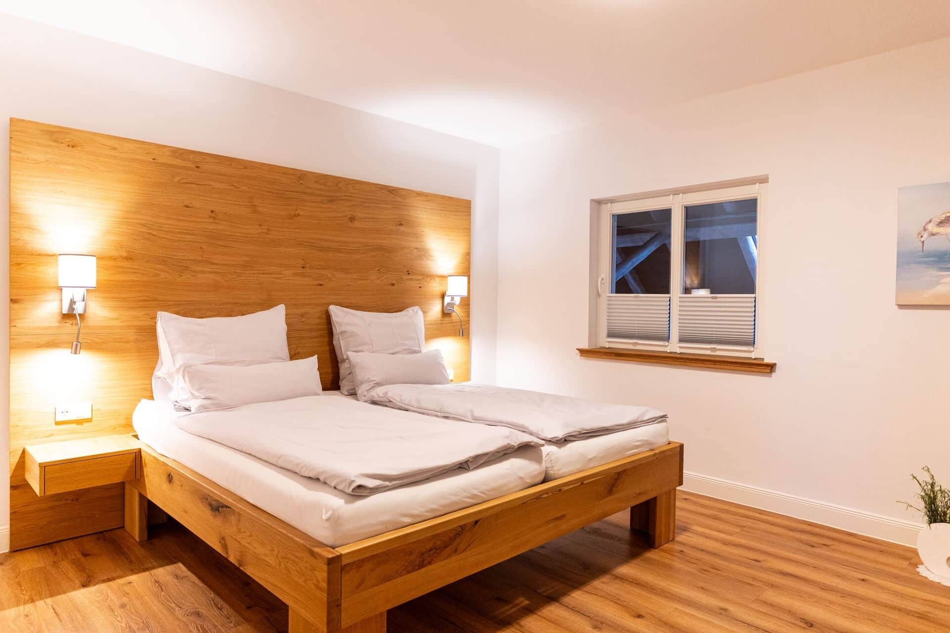 Ein Doppelbett mit Holzvorhang, Nachttischlampen und einem Fenster mit Jalousien.