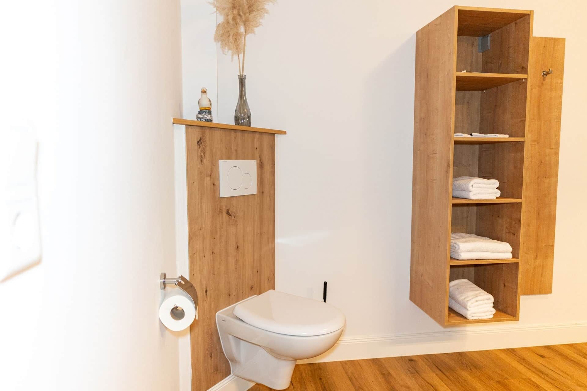 Ein Badezimmer mit Toilette, einem Holzregal mit Handtüchern und einem Toilettenpapierhalter.