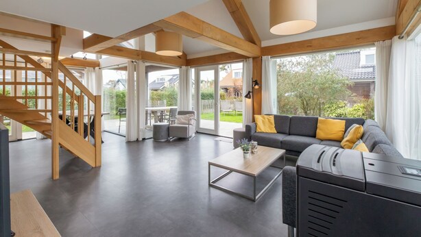 Ein geräumiger Wohnbereich mit einer Holztreppe, einem Sofa mit gelben Kissen, einem Couchtisch und einem großen Fenster mit Blick ins Freie.
