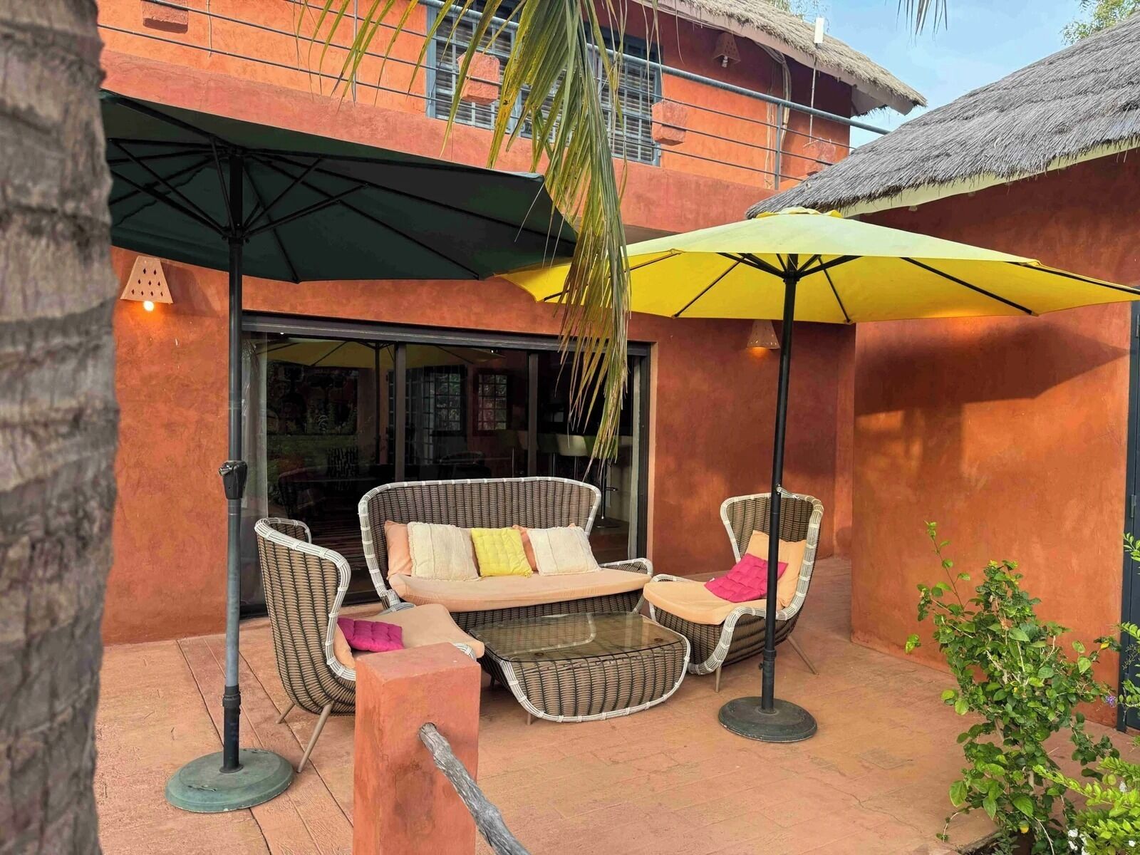 An outdoor seating area with wicker furniture and umbrellas, a glass door entrance, and a thatched roof structure.