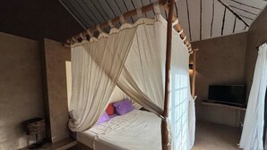 A single bed with a canopy, a television on a stand, and a shelf with a basket. - Villa Terre et Océan  (Ngaparou)