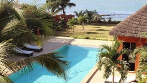 A pool area with lounge chairs, a thatched-roof structure, and a view of the ocean. - Villa Terre et Océan  (Ngaparou)