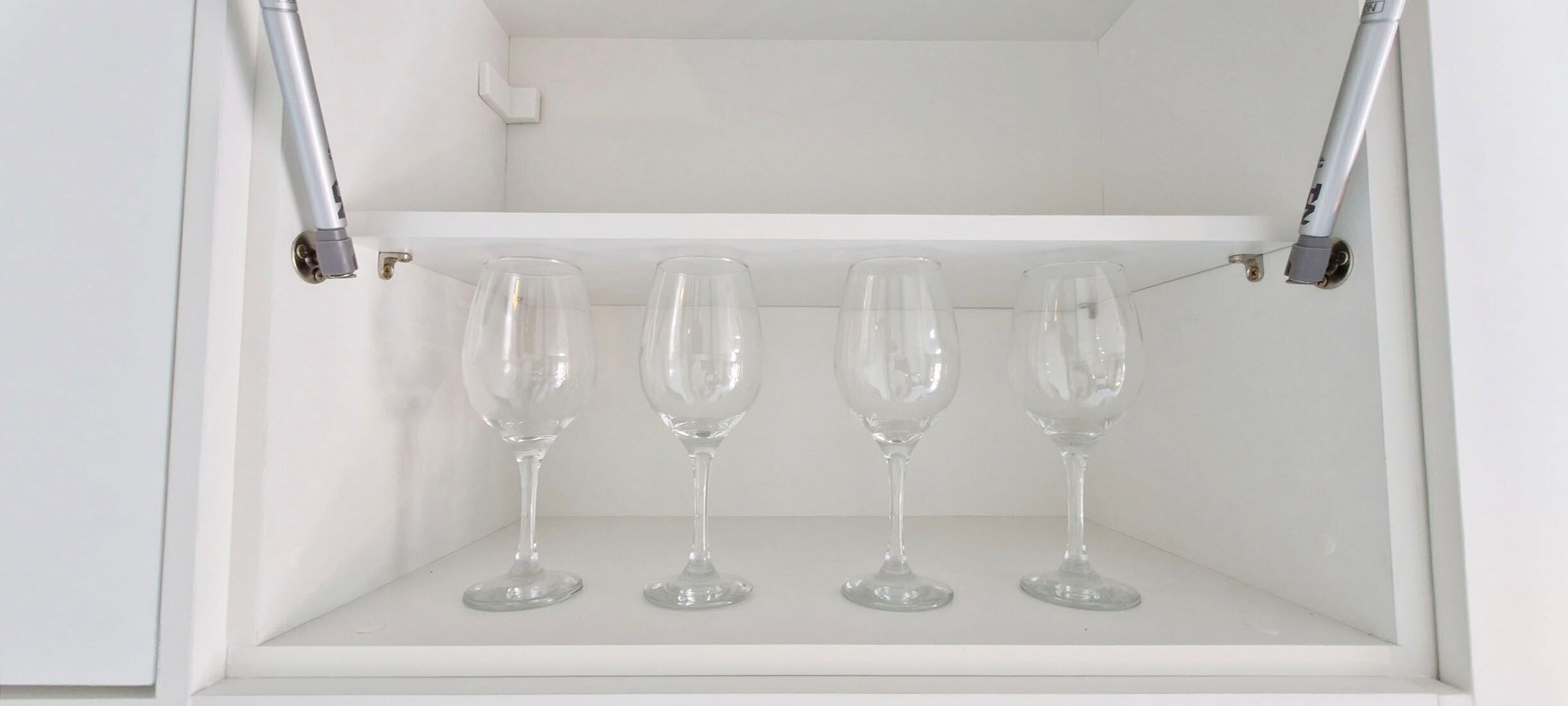 Un meuble blanc avec quatre verres à vin posés sur une étagère.