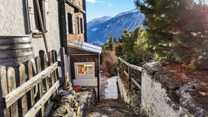 A narrow stone pathway leading to a small wooden structure with a window, surrounded by mountains and pine trees. - Maison Historique de Charme à Mollens, 8 pers (Mollens)