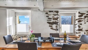 A dining area with a stone wall, two windows, and a table set for four. - Maison Historique de Charme à Mollens, 8 pers (Mollens)
