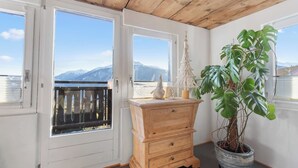 A balcony with a wooden ceiling, a wooden dresser, a potted plant, and a view of mountains through the windows. - Maison Historique de Charme à Mollens, 8 pers (Mollens)