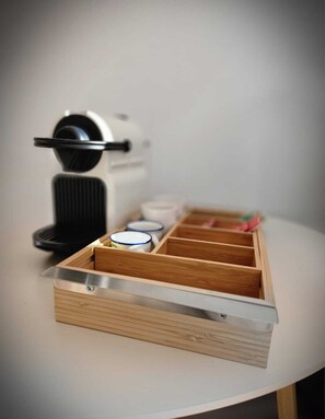 A wooden drawer organizer with compartments, a coffee maker, and a small white container on a table.