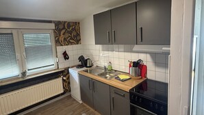 A compact kitchen with grey cabinets, a wooden countertop, a built-in oven, and a window with blinds. - Apartment in Troisdorf T06 (Troisdorf)