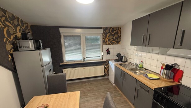 A compact kitchen with a dining table, a microwave, a kettle, and a sink. - Apartment in Troisdorf T06 (Troisdorf)