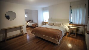 A bedroom with two beds, a bedside table with a lamp, a round mirror, and a window with curtains. - Hostería & Apart Hotel Carelhue (San Carlos de Bariloche)