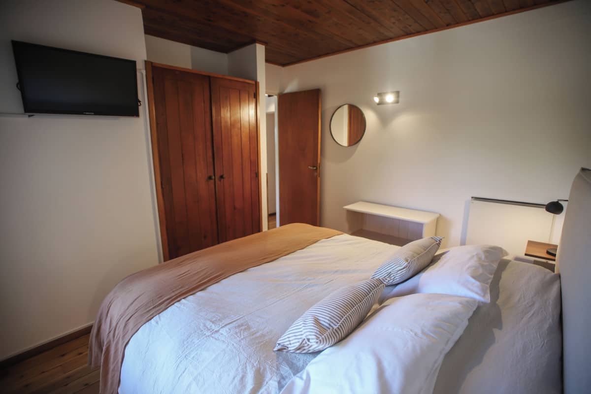 A bedroom with a bed, wooden wardrobe, a bedside table, a mirror, and a TV mounted on the wall.
