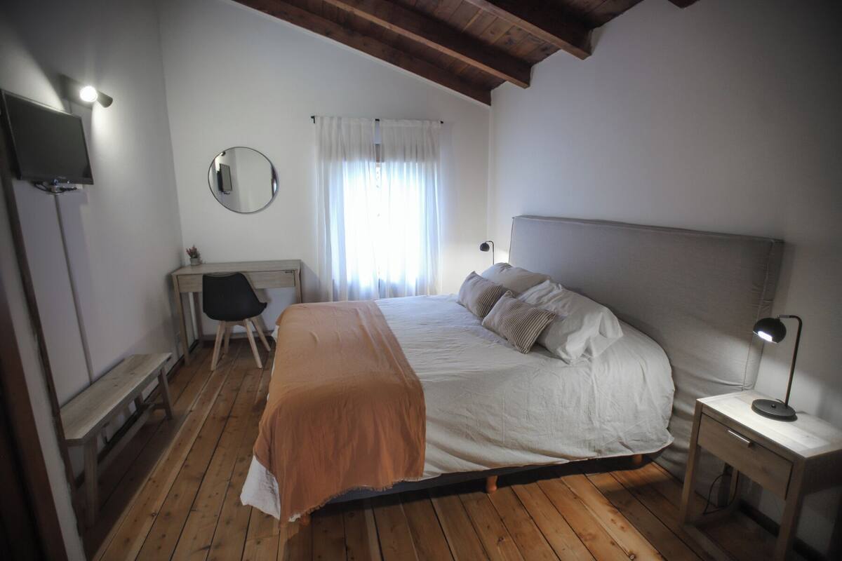 A bedroom with a bed, a desk, a chair, a mirror, and a lamp.
