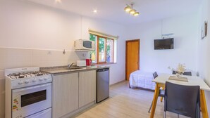 A compact kitchen with a gas stove, microwave, and dishwasher, a dining area with a table and chairs, and a bed in the adjacent room. - Hostería & Apart Hotel Carelhue (San Carlos de Bariloche)
