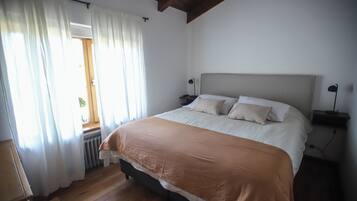 Een slaapkamer met een groot bed, witte gordijnen, een houten vloer en een raam met uitzicht.